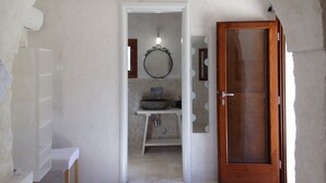 Un pasillo estrecho que lleva a un baño con lavamanos, espejo y una puerta de madera.