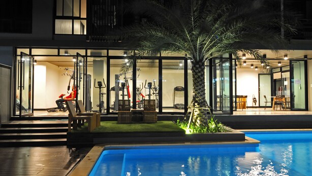 A modern house with a swimming pool, glass doors leading to a patio, and outdoor furniture. - Grand Marina Residence (Si Racha)