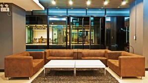 A modern lobby with a sectional sofa, a white coffee table, and a glass partition with a view of an indoor dining area. - Grand Marina Residence (Si Racha)