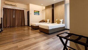 A hotel room with two beds, a wooden floor, an air conditioning unit, a painting, and a desk. - Grand Marina Residence (Si Racha)