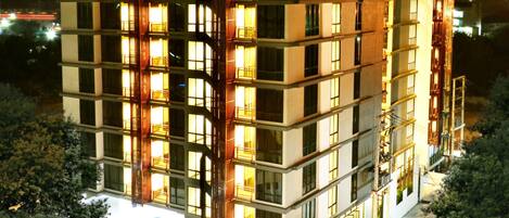 A multi-story hotel with balconies, a parking area, and a pool.