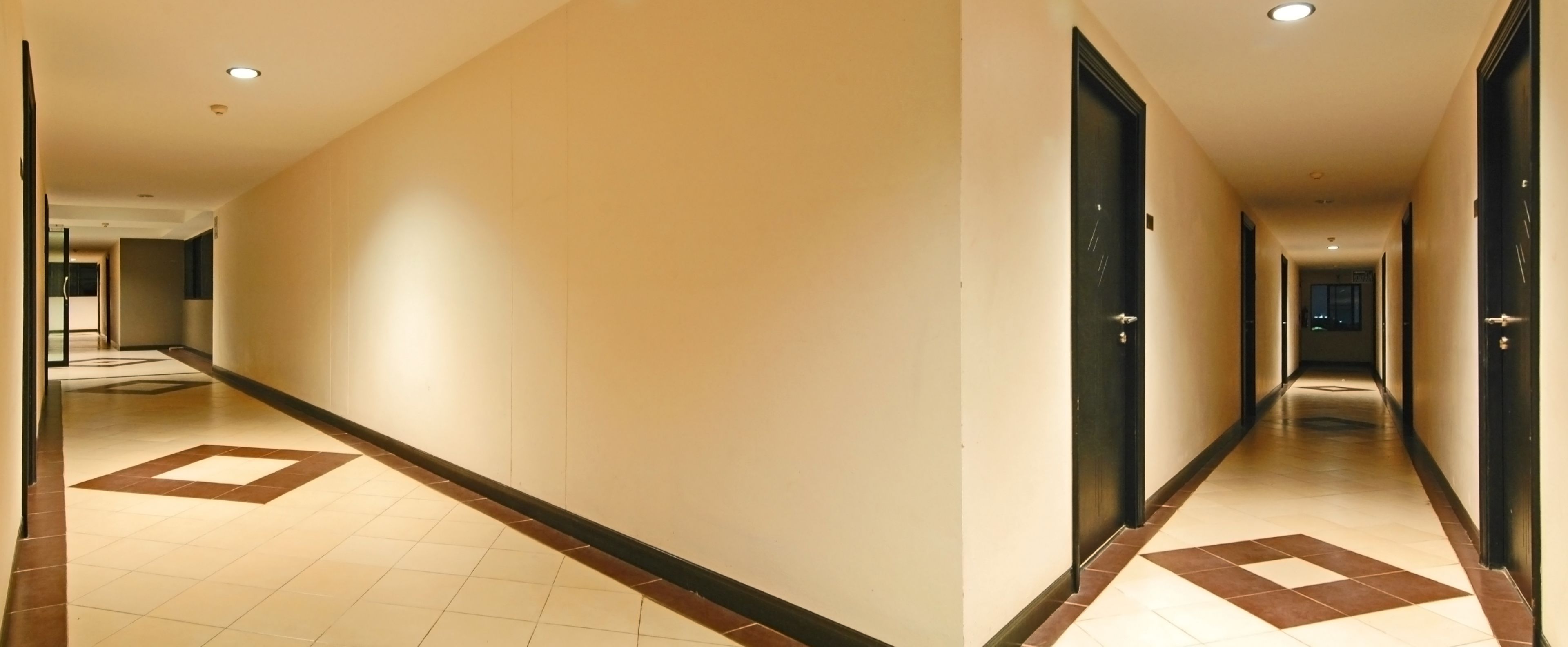 A long, narrow hotel corridor with tiled floors and dark-colored doors.