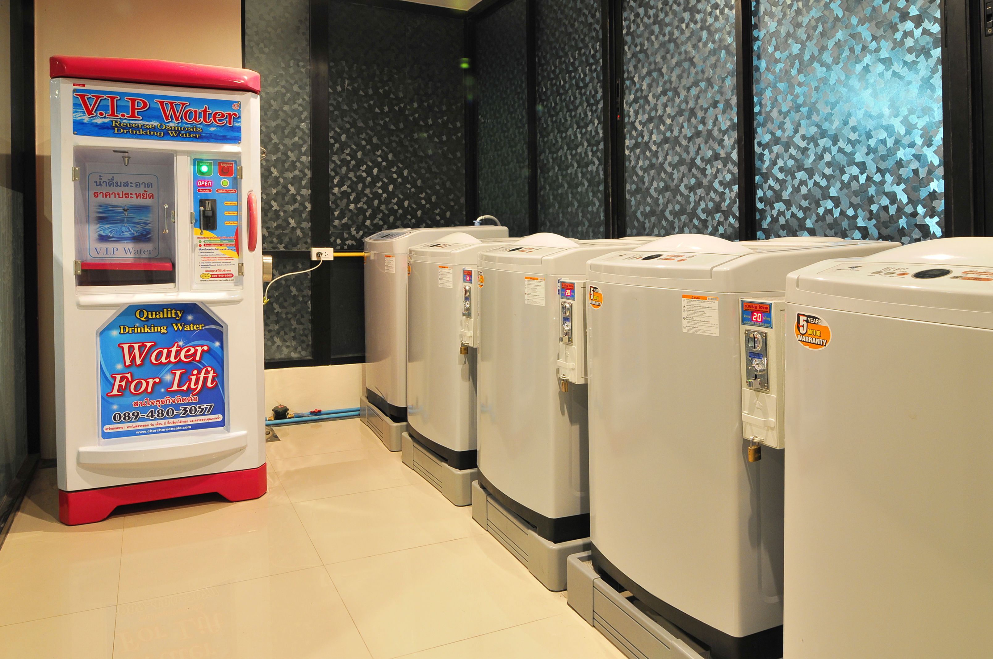 Um dispensador de água e vários aquecedores de água em um espaço com piso de azulejos e paredes estampadas.