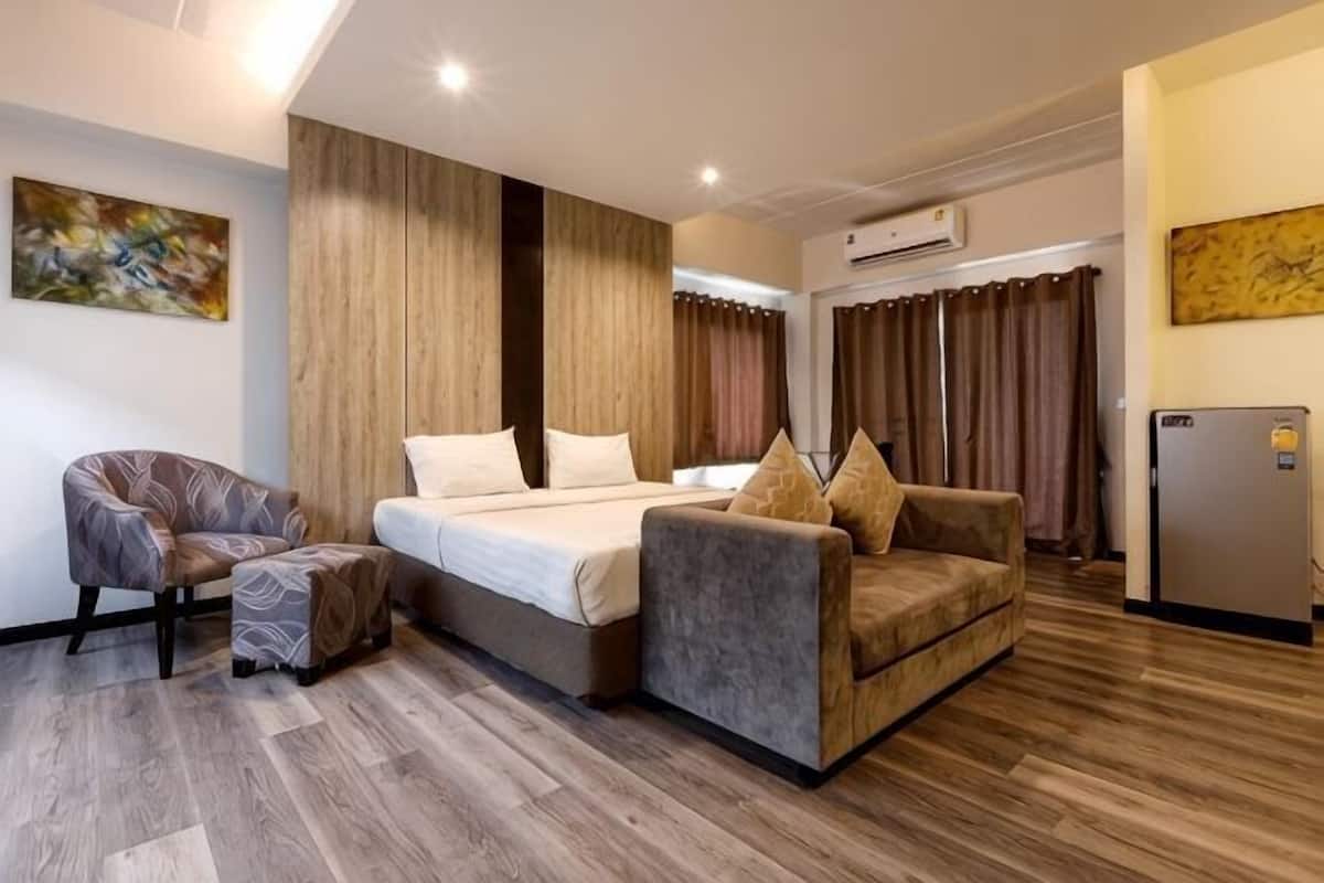 Une chambre d’hôtel comprenant un lit, deux fauteuils, une petite table et un réfrigérateur.