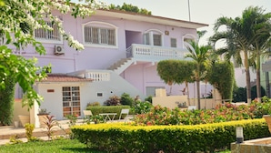 Um edifício rosa com varanda, escadaria e um jardim bem cuidado com diversas plantas e flores.