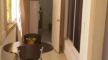 A narrow hallway with a dining table and chairs, a large window, and a door leading to another room.