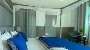 Quarto de hotel com duas camas, uma escrivaninha, uma cadeira e uma pequena mesa com uma planta.