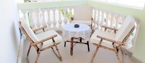 A corner balcony with two white cushioned chairs and a small round table with a floral tablecloth. - Pelican Residence (Bakau)