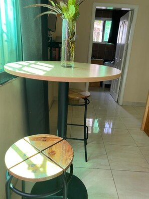 A round dining table with a glass top and a stool with a patterned seat. A clear vase with a plant is on the table. - Pelican Residence (Bakau)