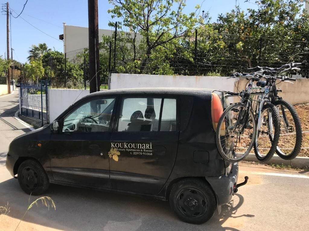 Un coche compacto con una bicicleta sujeta en la parte trasera, estacionado en una calle.
