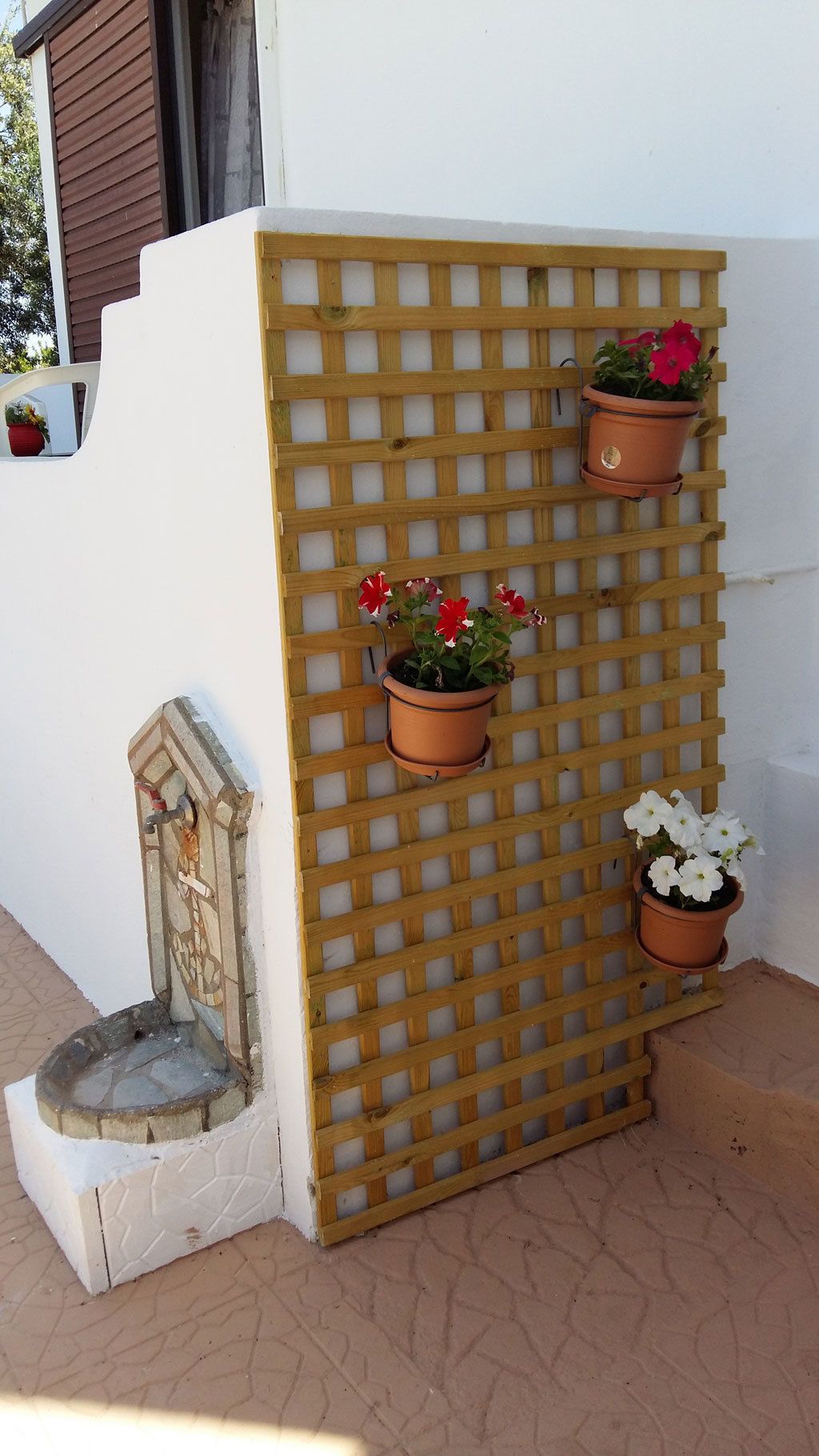 A wooden lattice wall with three terracotta pots containing flowers.