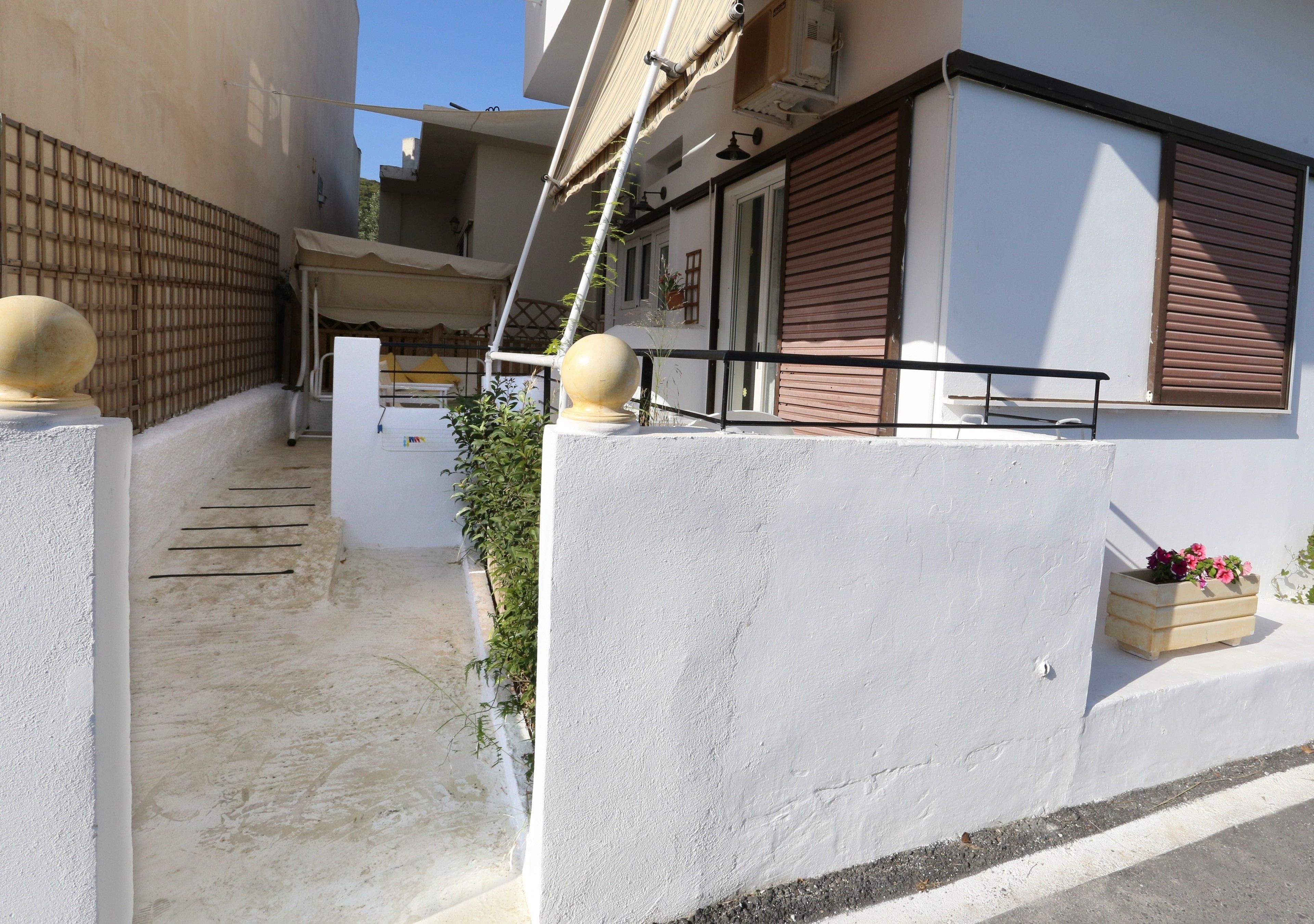 Un edificio residenziale con facciata bianca, un balcone con ringhiera color beige e una recinzione in legno.