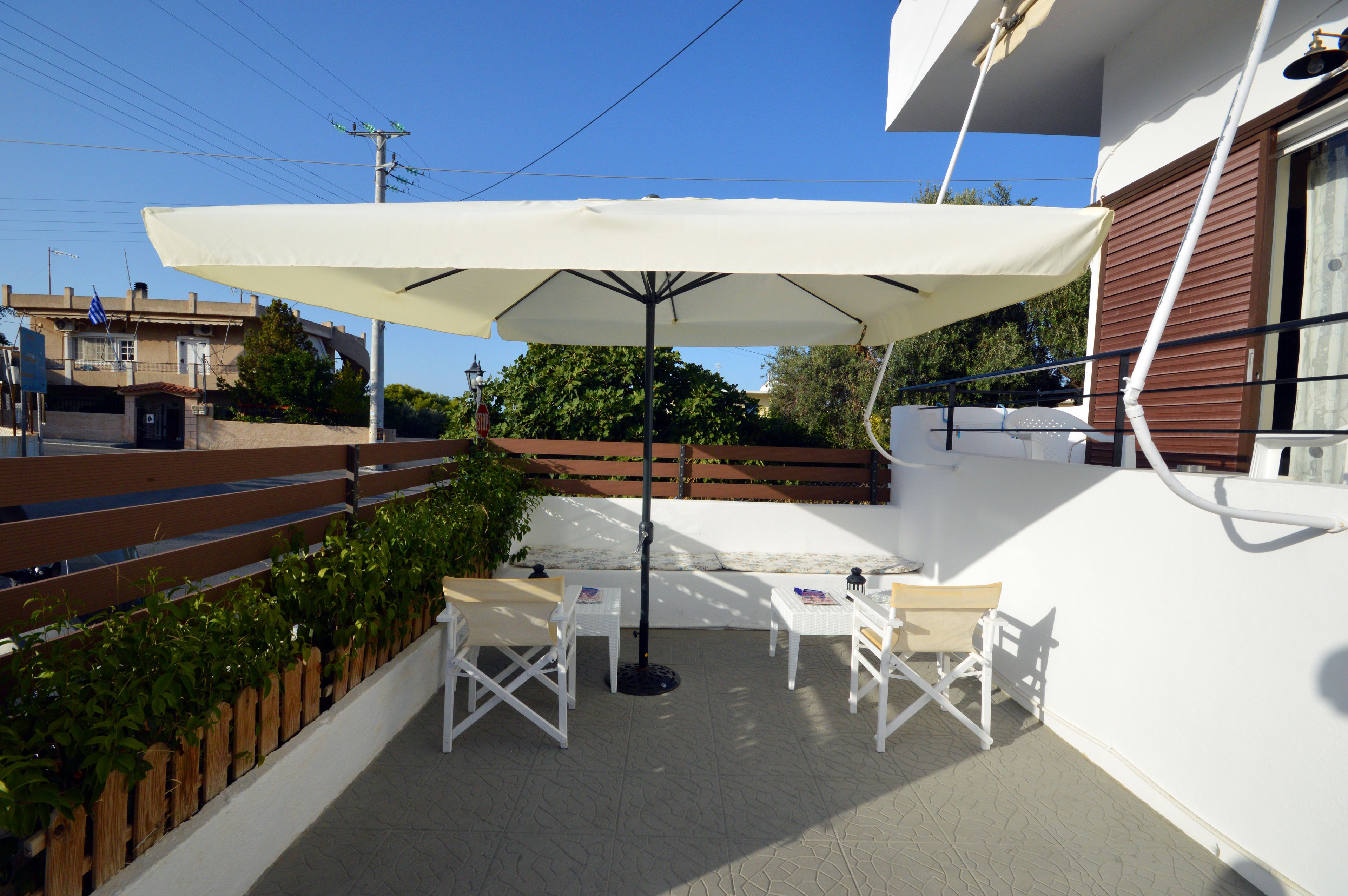 Eine Außenpatio mit weißen Korbmöbeln, einem großen weißen Sonnenschirm und einem Holzzaun.