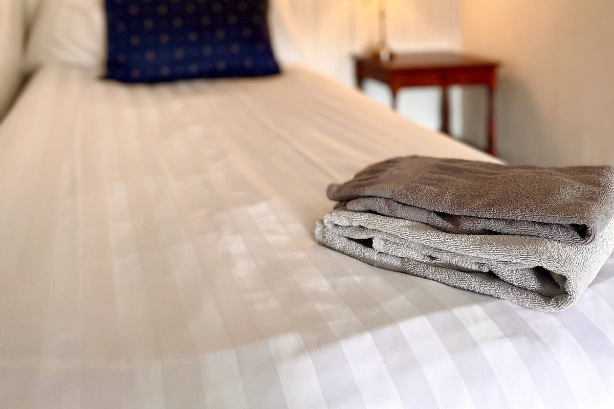 Une pièce chaleureuse et faiblement éclairée, avec un lit, des oreillers et une serviette pliée.