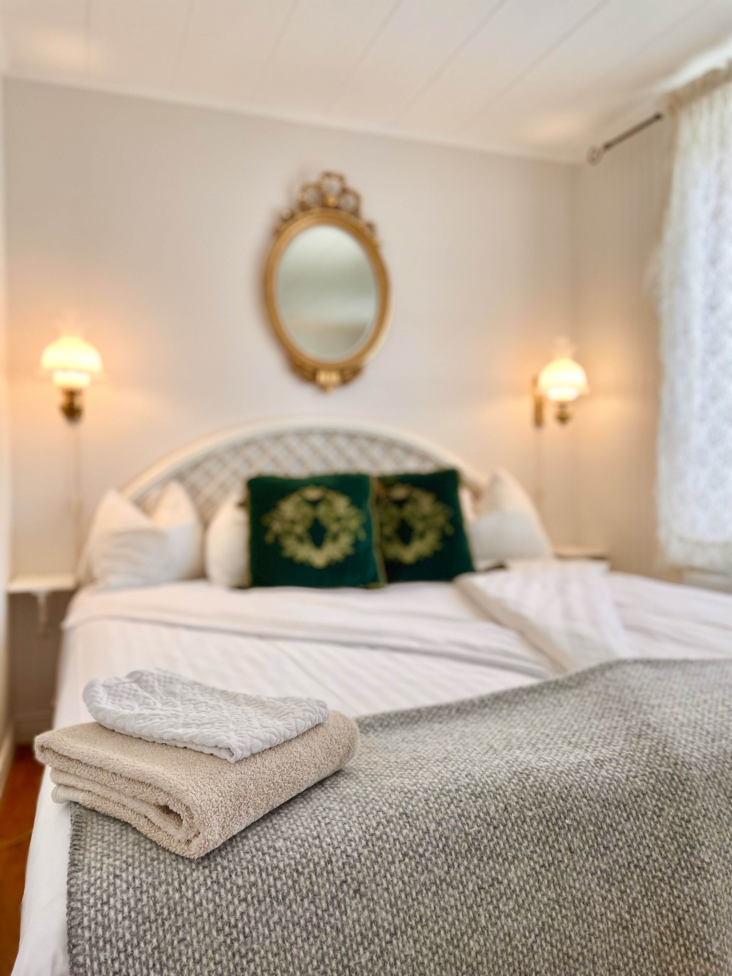 Una cama bien hecha con una toalla doblada, dos almohadas decorativas y un espejo en la pared.