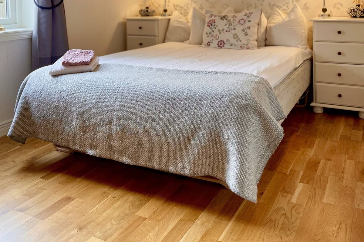 Une chambre à coucher bien rangée, avec un grand lit, deux tables de chevet, une commode et une fenêtre avec des rideaux.