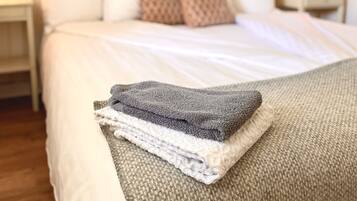 A neatly made bed with a folded blanket, a patterned wall, and a bedside lamp.