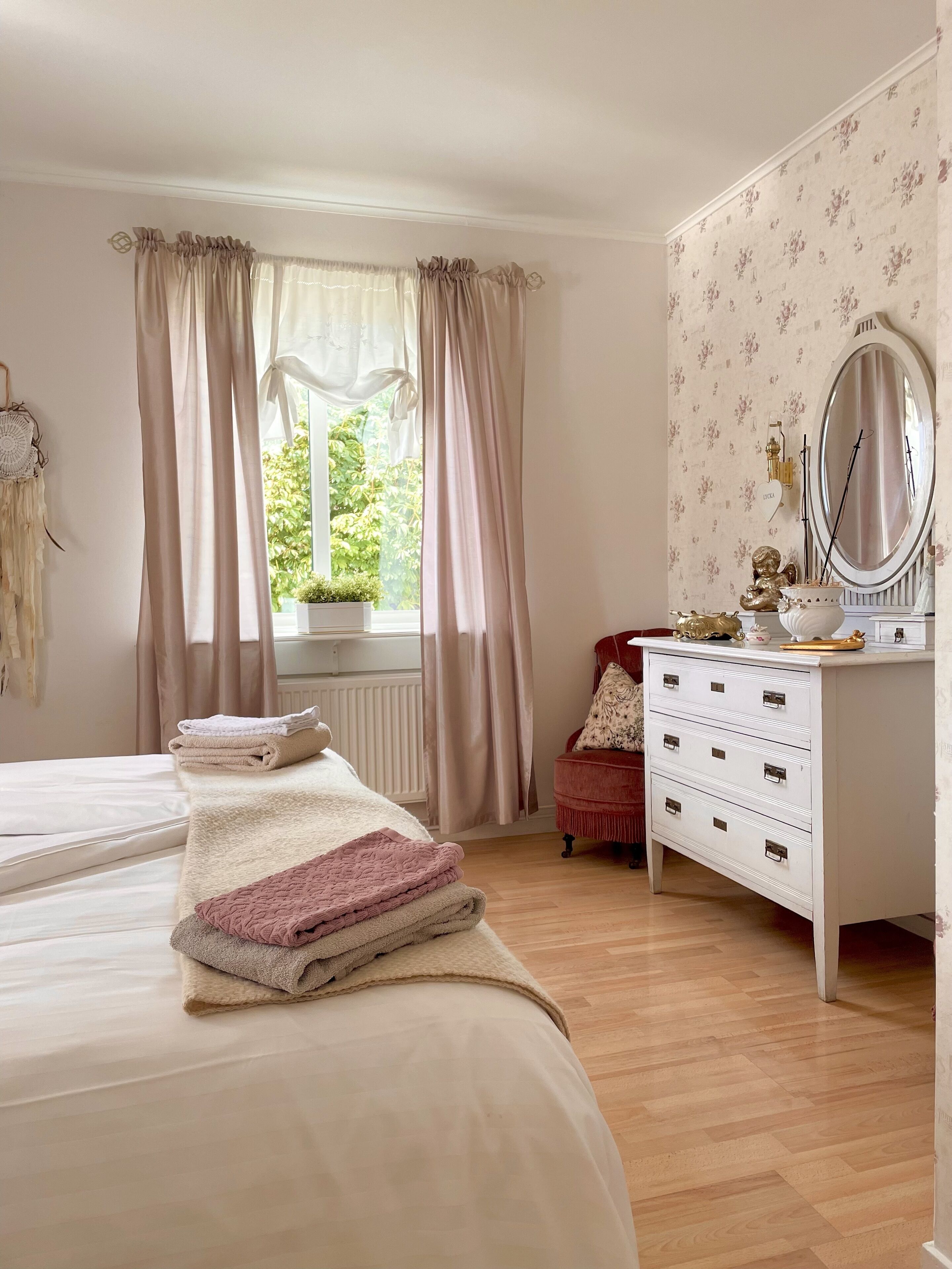 Une chambre à coucher comprenant un lit, une commode, une coiffeuse avec un miroir et une fenêtre avec des rideaux.