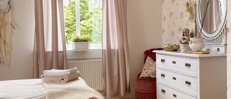 Une chambre à coucher comprenant un lit, une commode, une coiffeuse avec un miroir et une fenêtre avec des rideaux.