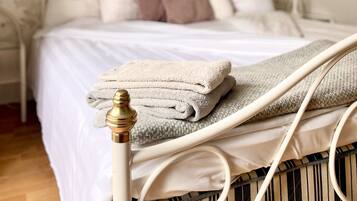 Una cama bien hecha con ropa de cama blanca y una toalla doblada sobre una estructura de metal.