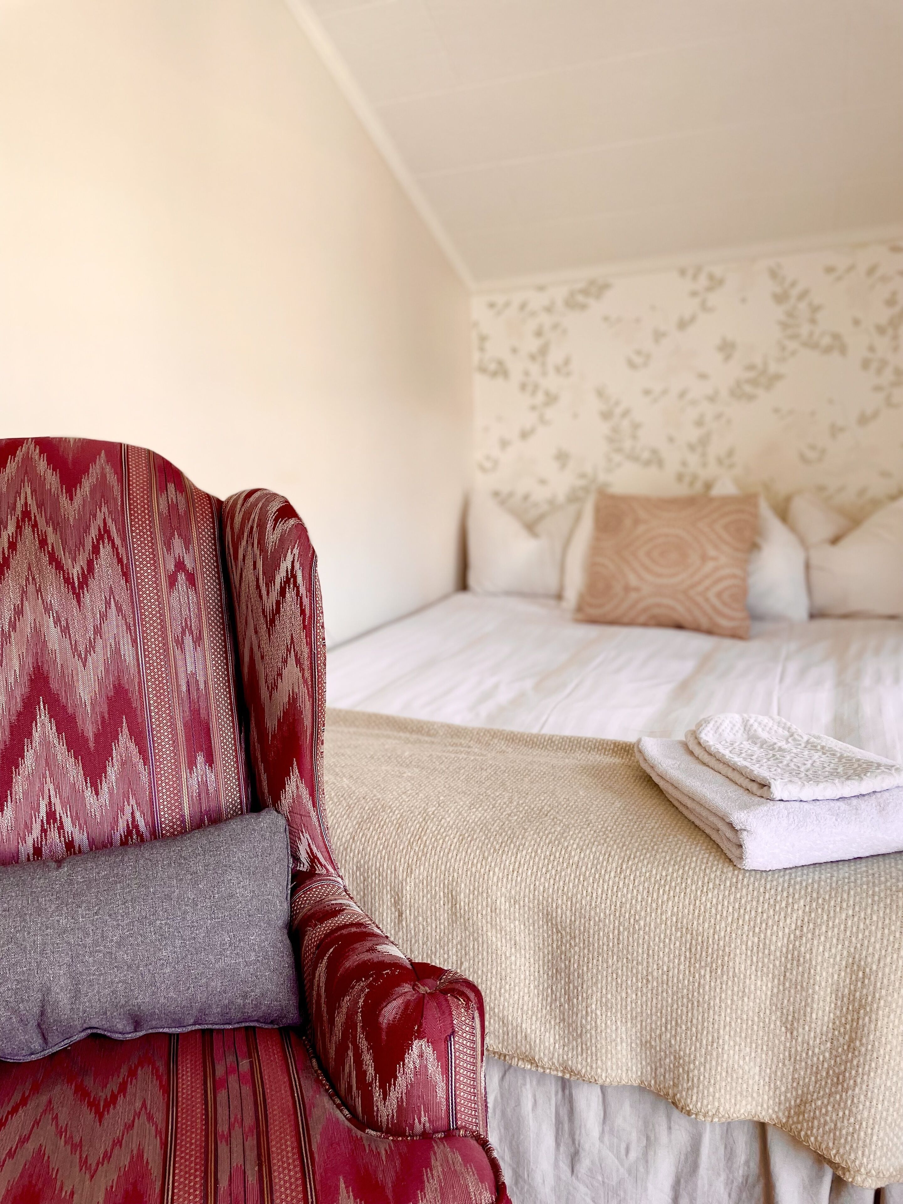 A bedroom with a bed, pillows, a blanket, and a chair.