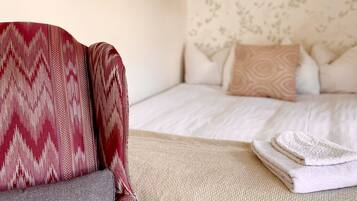 A bedroom with a bed, pillows, a blanket, and a chair.