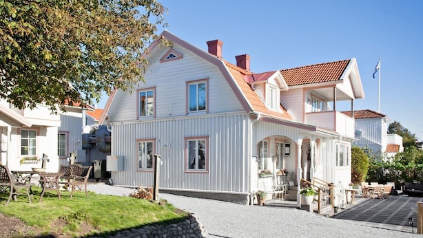 Une maison à deux étages avec un toit en pente, un porche à l’avant et une allée gravillonnée.