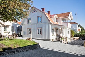Une maison à deux étages avec un toit en pente, un porche à l’avant et une allée gravillonnée.