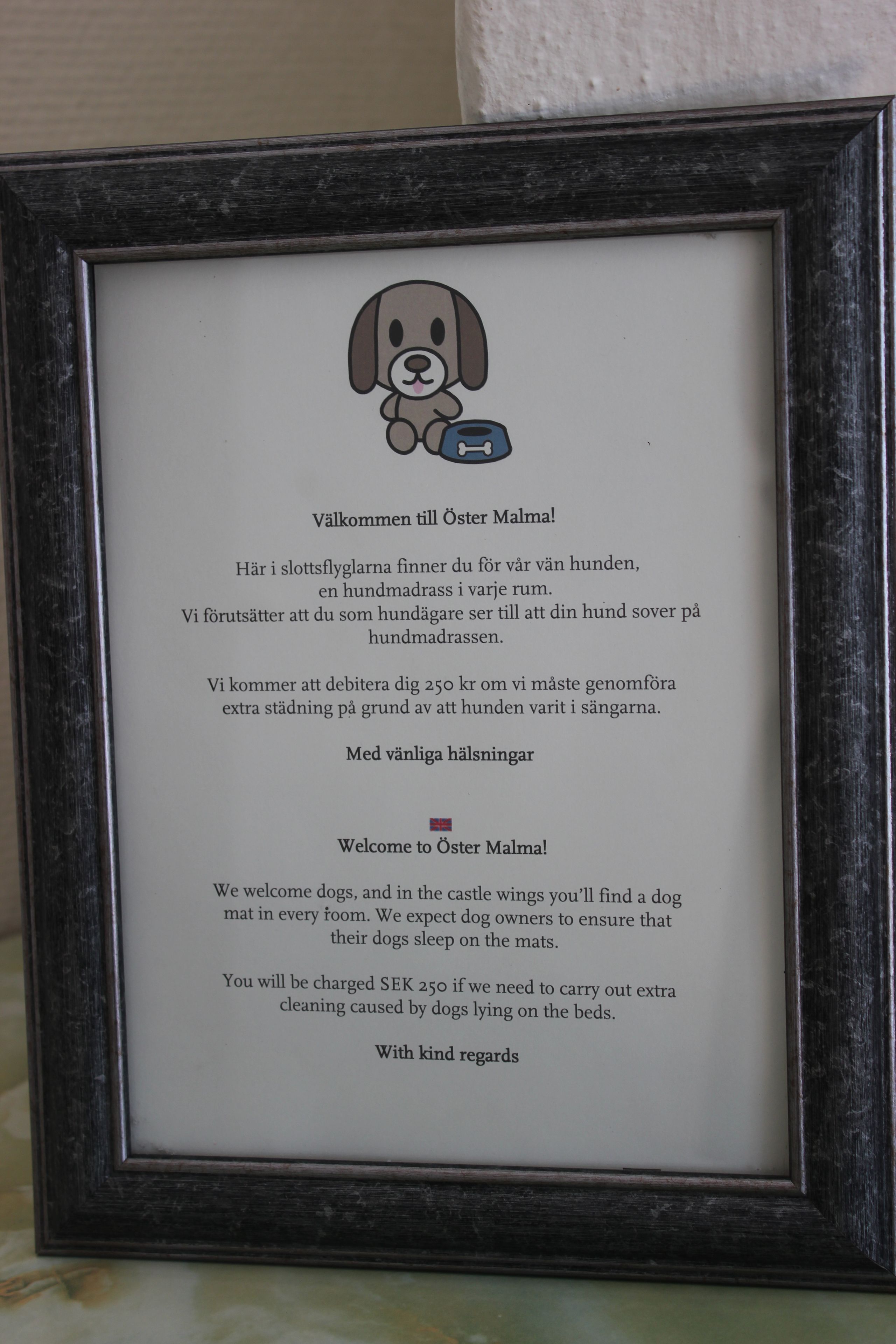 A framed welcome message for dogs in a castle, including a dog illustration and text in Swedish and English.