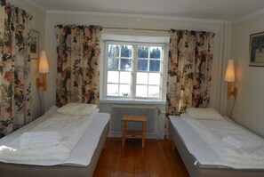 Quarto com duas camas, um banquinho de madeira e uma janela com cortinas.