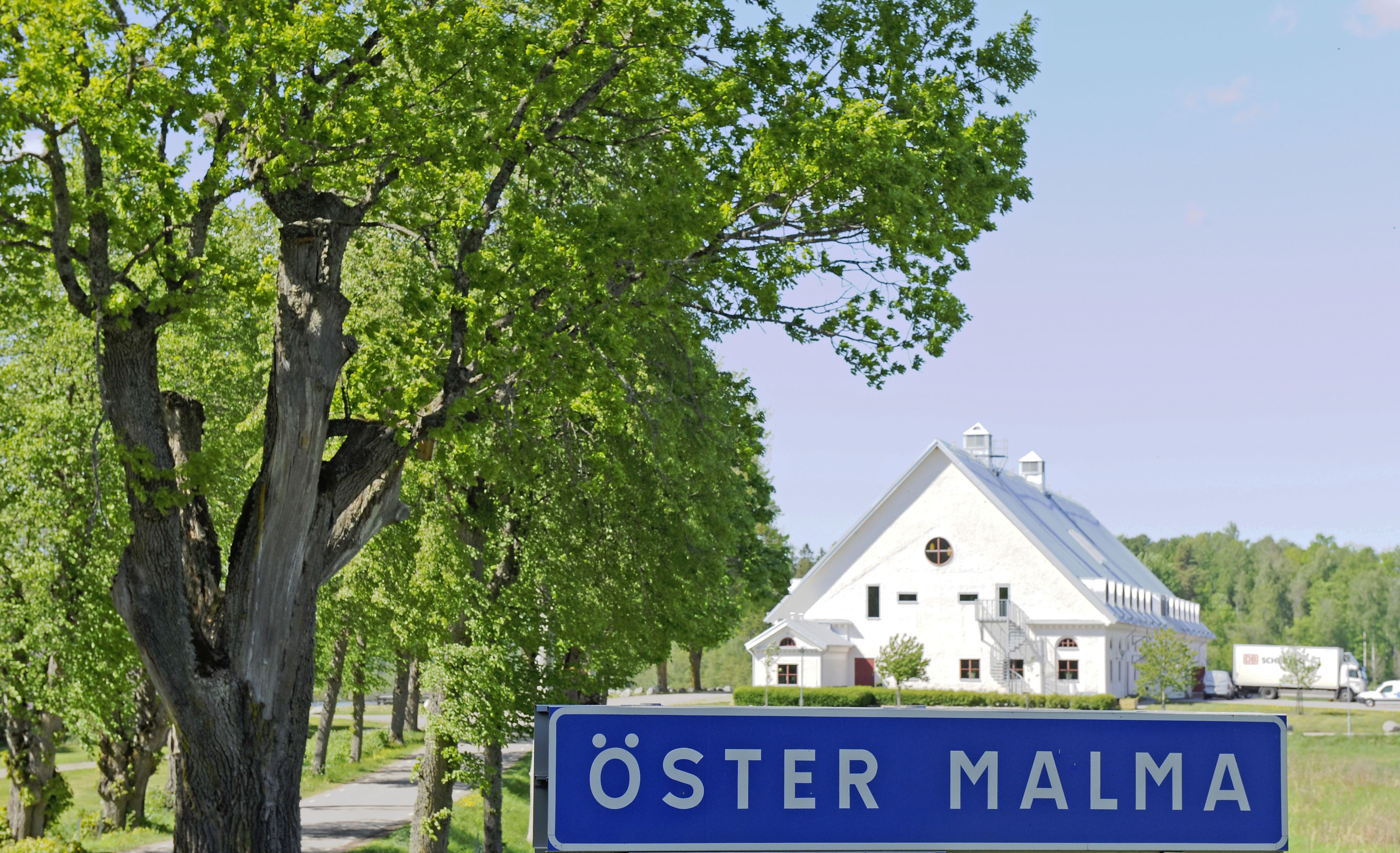 En stor vit byggnad med ett sluttande tak, omgiven av träd och en klar himmel.