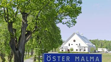 En stor vit byggnad med ett sluttande tak, omgiven av träd och en klar himmel.