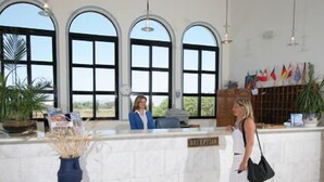 A reception area with a marble counter, large arched windows, and a display of flags. - Nina Beach Hotel (Kos)