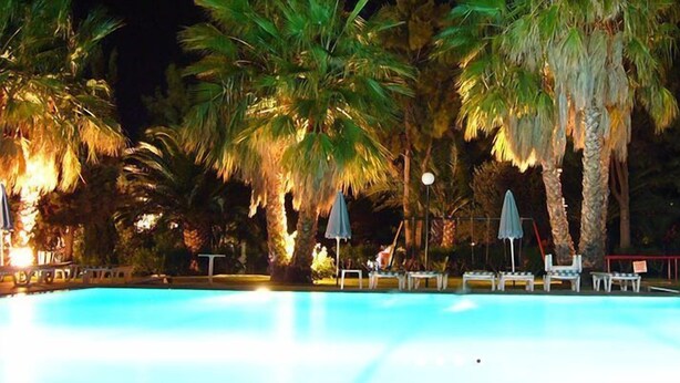 A swimming pool with lounge chairs and umbrellas, surrounded by palm trees. - Nina Beach Hotel (Kos)