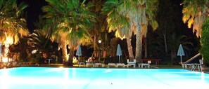 En swimmingpool med solstolar och parasoller, omgiven av palmer.