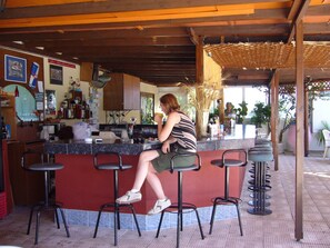 A bar area with a counter, stools, and a person sitting. - Nina Beach Hotel (Kos)
