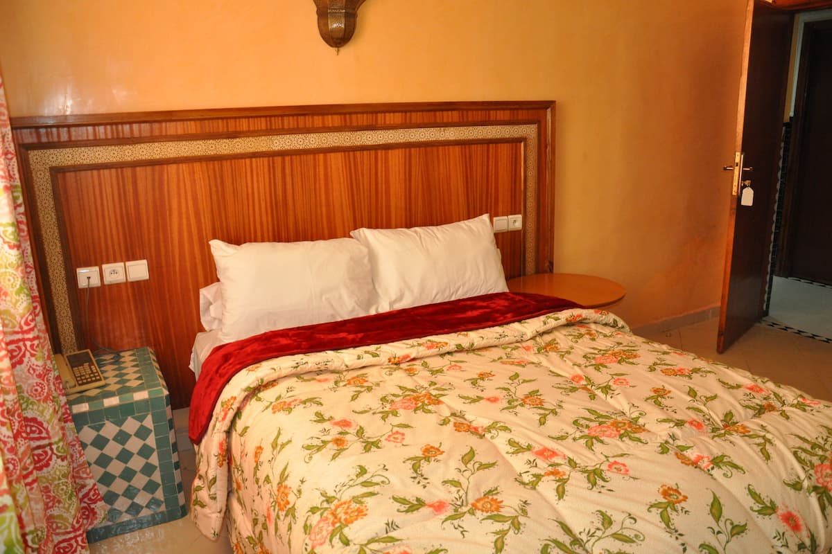 A bed with a floral bedspread, a wooden headboard, and a red throw blanket.