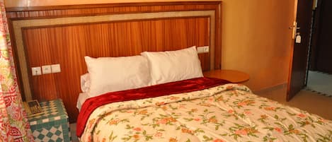 A bed with a floral bedspread, a wooden headboard, and a red throw blanket.