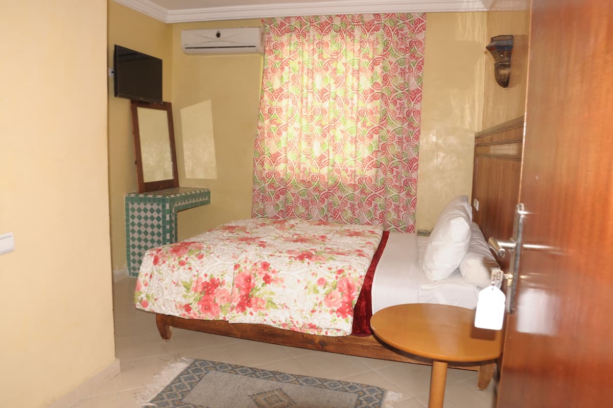 A bedroom with a bed, a bedside table, a mirror, and a curtain.