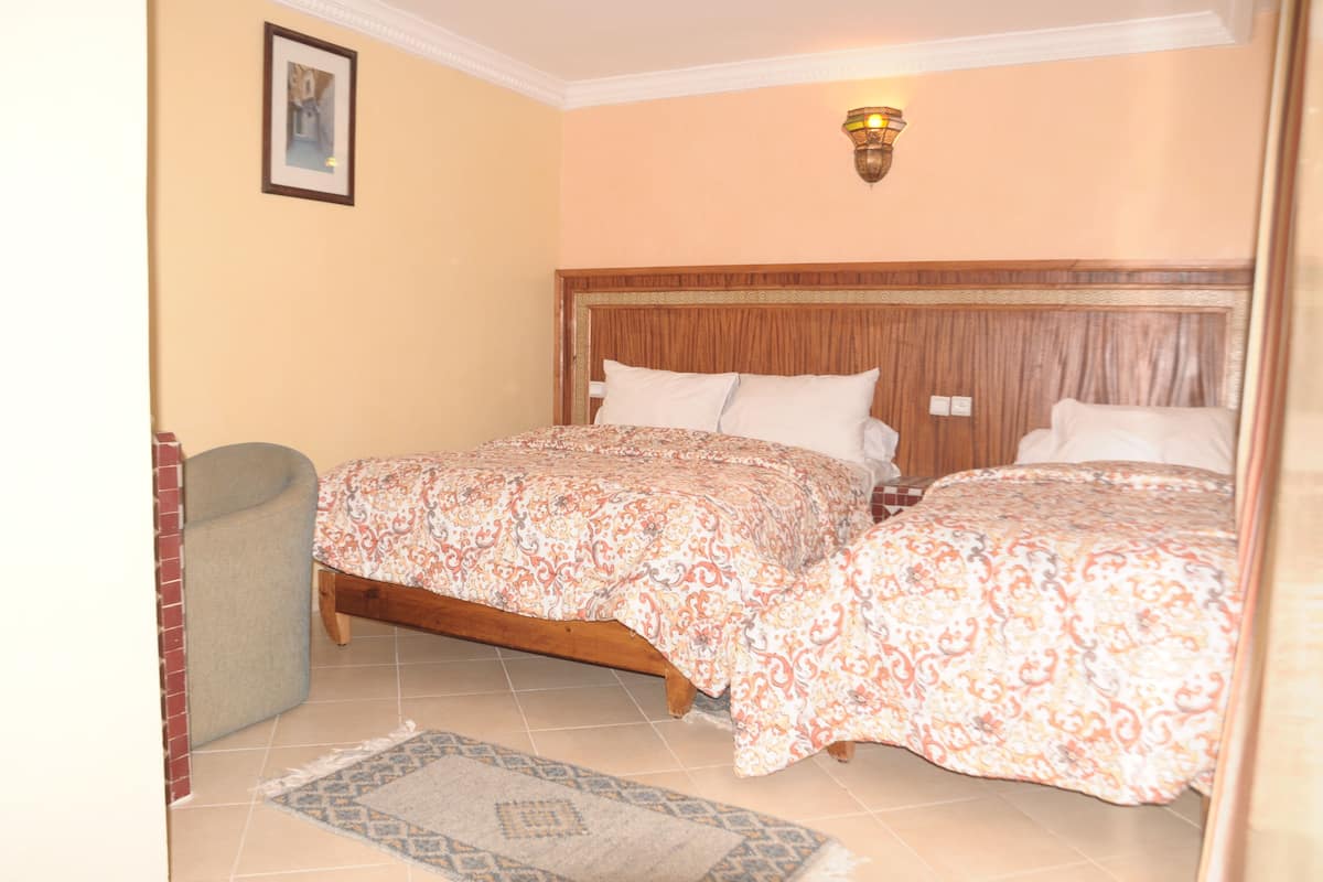 A bedroom with two beds, a wooden headboard, a patterned bedspread, a small rug, and a picture on the wall.