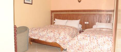 Un dormitorio con dos camas, cabecero de madera, colcha estampada, una alfombra pequeña y un cuadro en la pared.