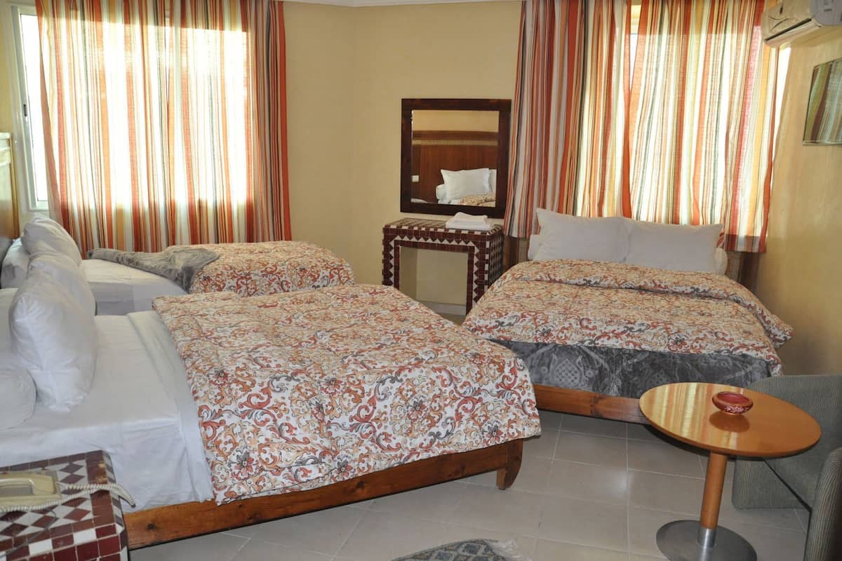 A hotel room with two beds, a small table, a chair, a mirror, and a telephone.