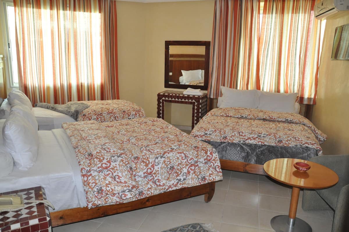 A hotel room with two beds, a small table, a chair, and a mirror.