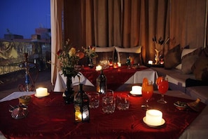 A dimly lit dining area with a red tablecloth, candles, and a variety of table settings including glasses and a bottle. - Riad Shaloma (Marrakech)