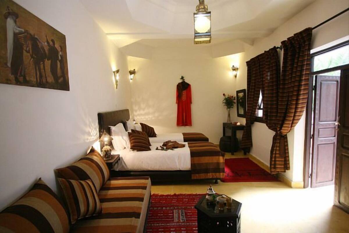 Habitación de hotel con cama, sofá, cortina roja y un cuadro en la pared.