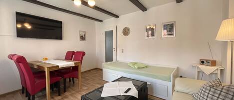 Un espacio habitable compacto con zona de comedor, cama, televisor y radio.