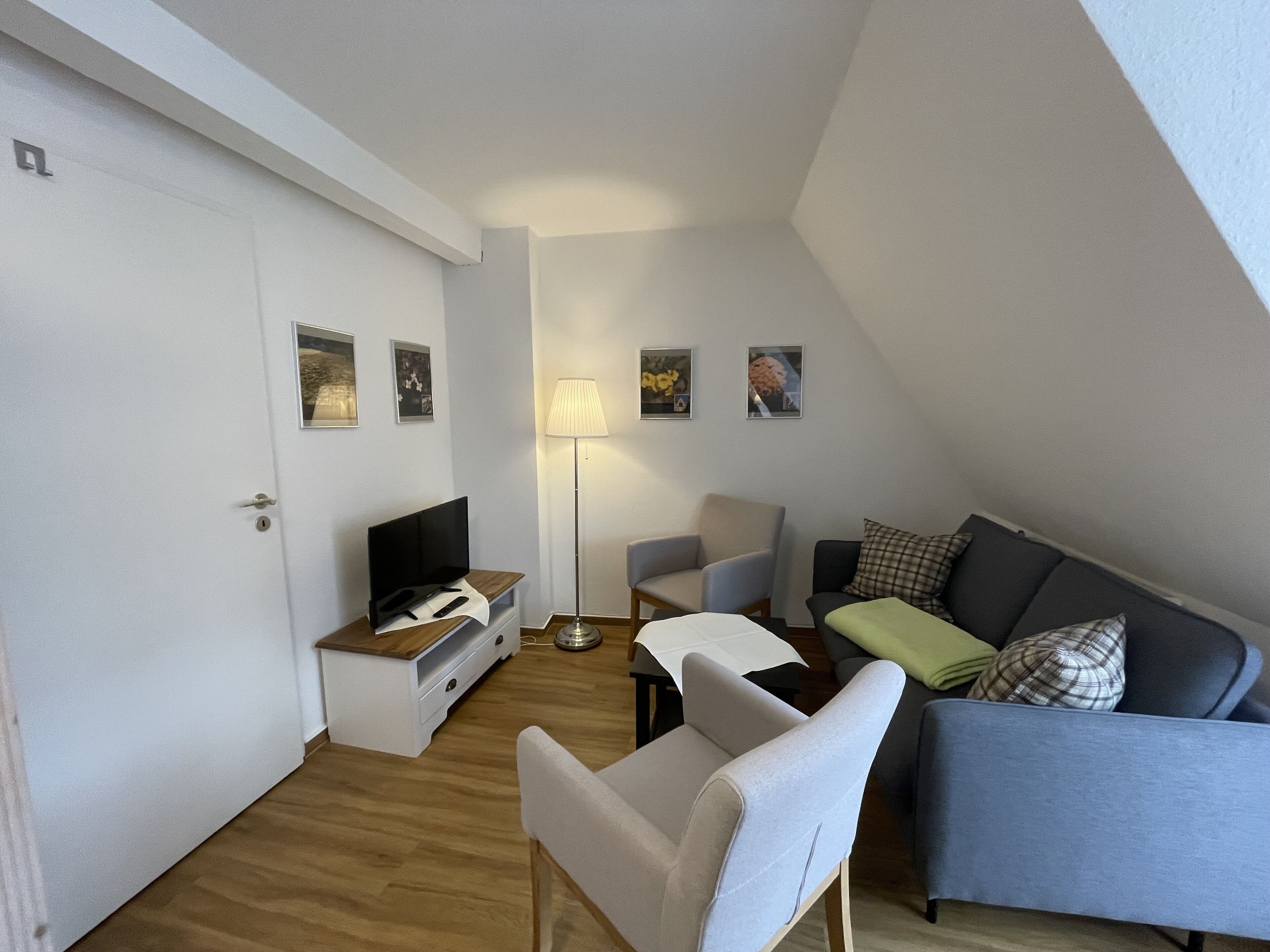 Un petit salon moderne doté d’un téléviseur à écran plat, d’un canapé, d’un fauteuil et d’une lampe.