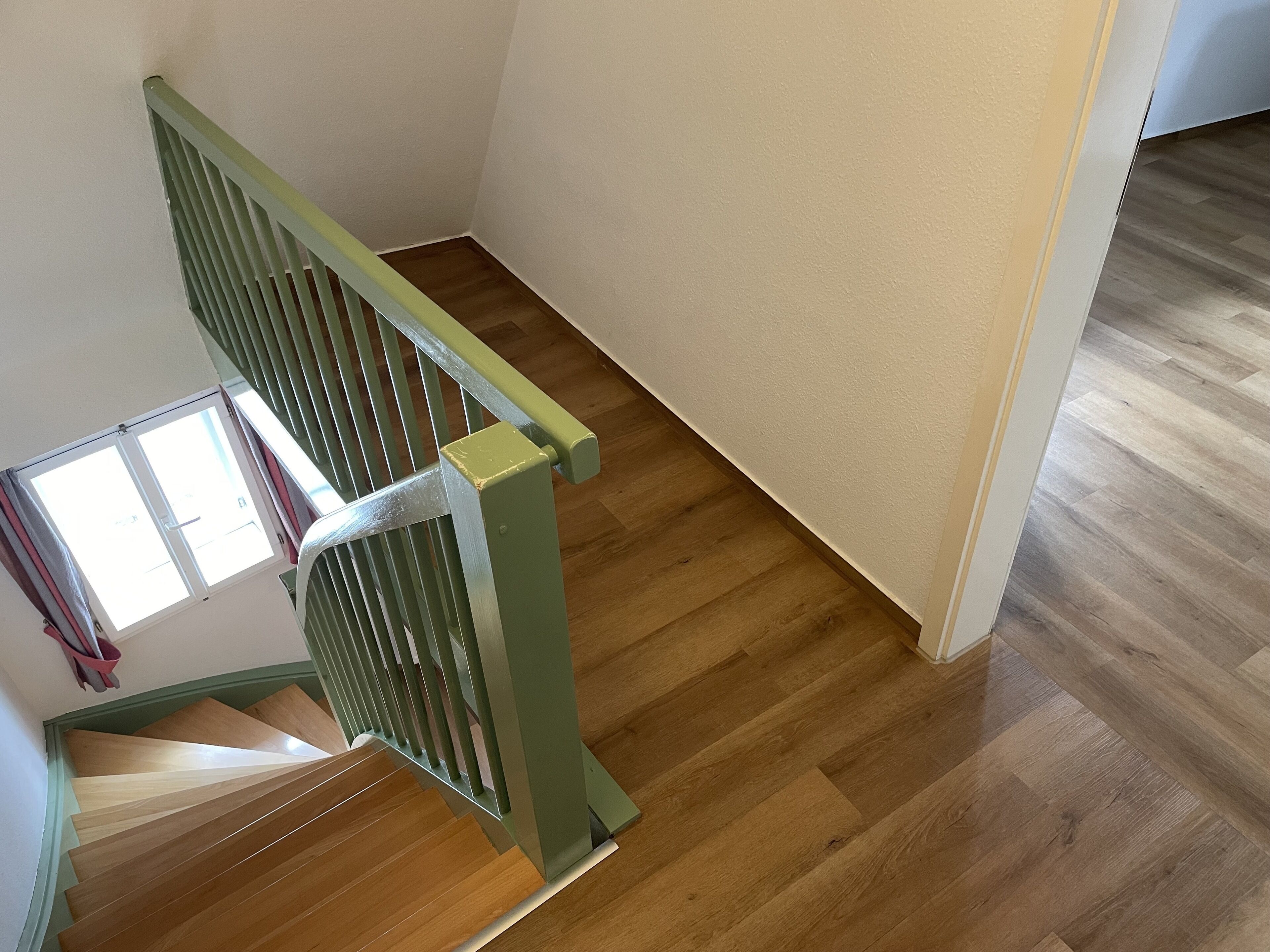 A wooden staircase with a green handrail leading to a landing.