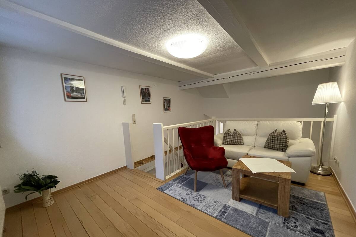 A living room with a red chair, a white sofa, a wooden coffee table, and a patterned rug.