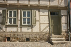Ein Gebäude mit einer Stein-Fassade, einer Holztreppe, die zu einer Tür führt, und einem Fenster mit einem Rollo.
